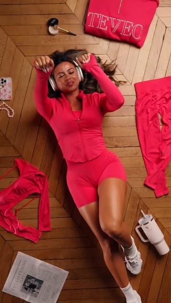 A high-angle, top-down shot of a model lying on a wood floor surrounded by an athleisure set, headphones, and daily essentials, utilizing a consistent color palette.